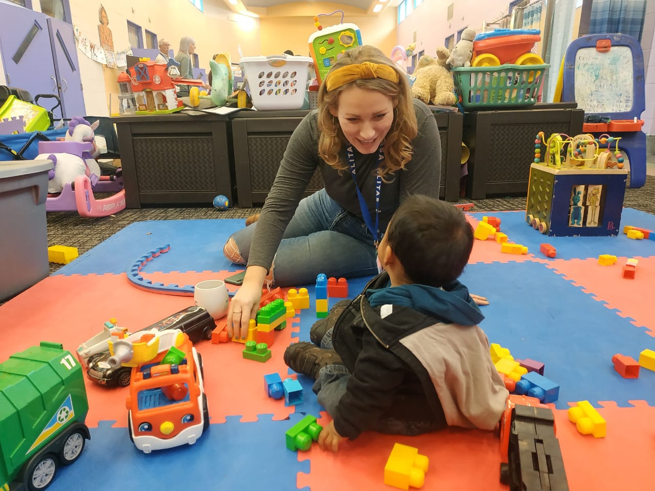 A smiling person sits on the floor with a small child.